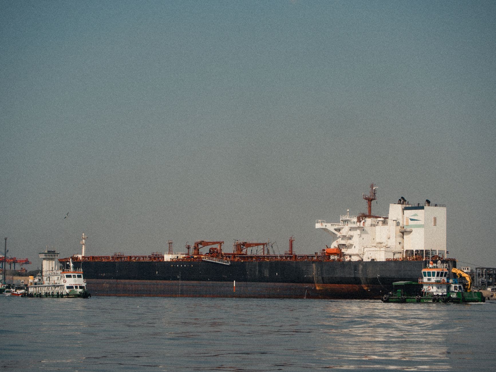 A cargo ship docked at a port with tugboats assisting on a clear day.